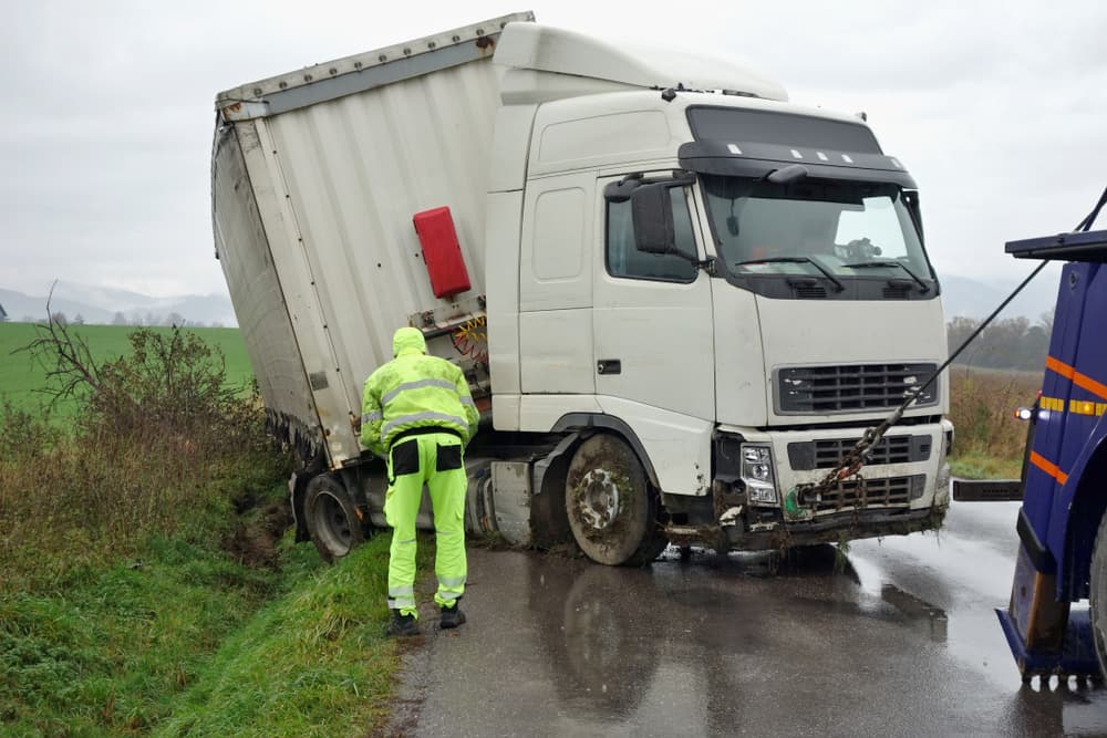 The truck lies in a ditch after the road accident over raining day in autumn time.