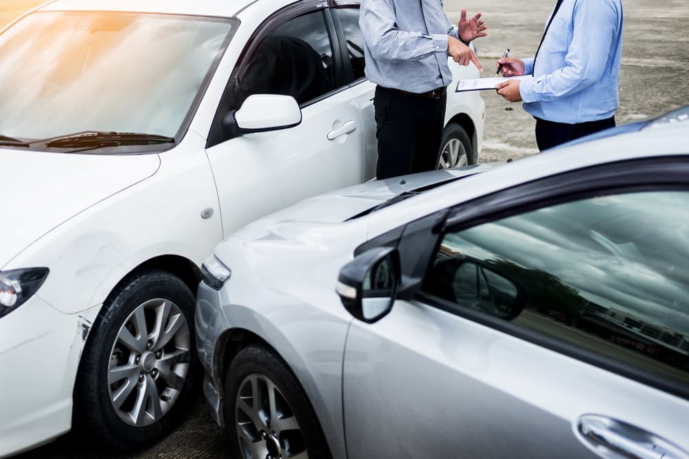 An insurance agent is writing on a clipboard while examining a car after an accident, assessing and processing the claim.