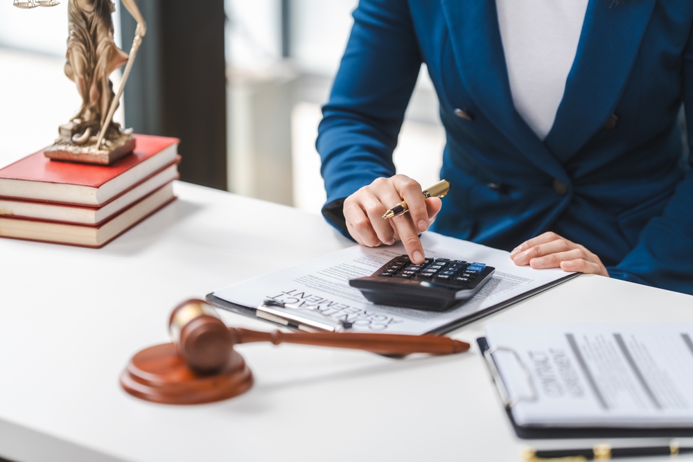 Here’s an updated version of the alt text: Close-up of a personal injury lawyer calculating costs with a legal contract, gavel, and law books on the table.